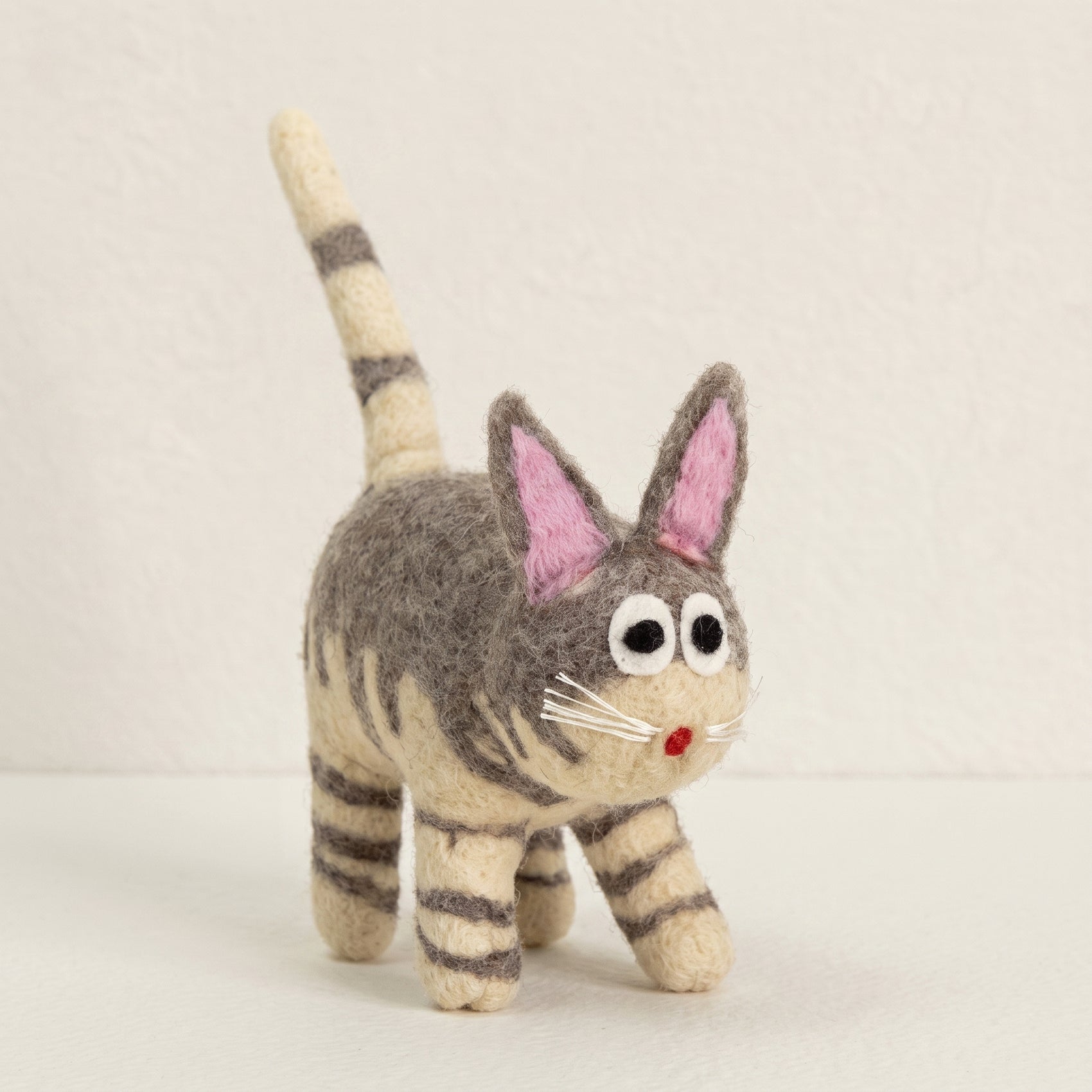 Hand-felted grey tabby cat with an upright striped tail, pink ears and wide eyes, on a white background