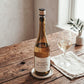 The Rattan Bottle Stopper seated in a white wine bottle on a rustic wood table, showing its compact size in use