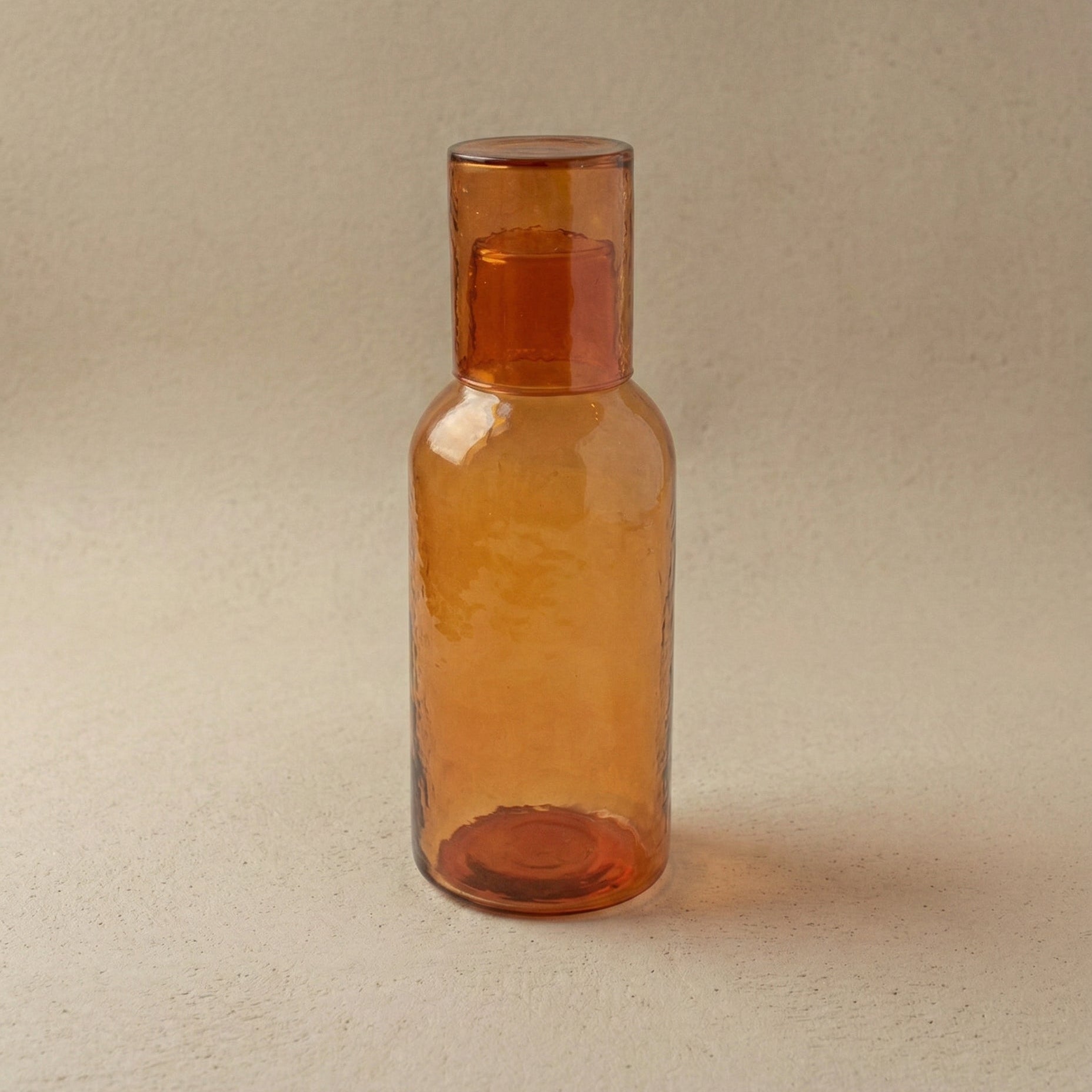 Hand-hammered recycled glass carafe in amber with tumbler lid, showing warm golden tones and hammered facets