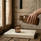 Hand-hammered recycled glass carafe in smoke gray with tumbler lid, showing cool tones and faceted texture