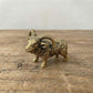The Resilient Presence miniature brass ram with coiled horns standing firm, showing warm aged patina and textured detail on a wooden surface, from the WILLAGE Tiny Objects collection