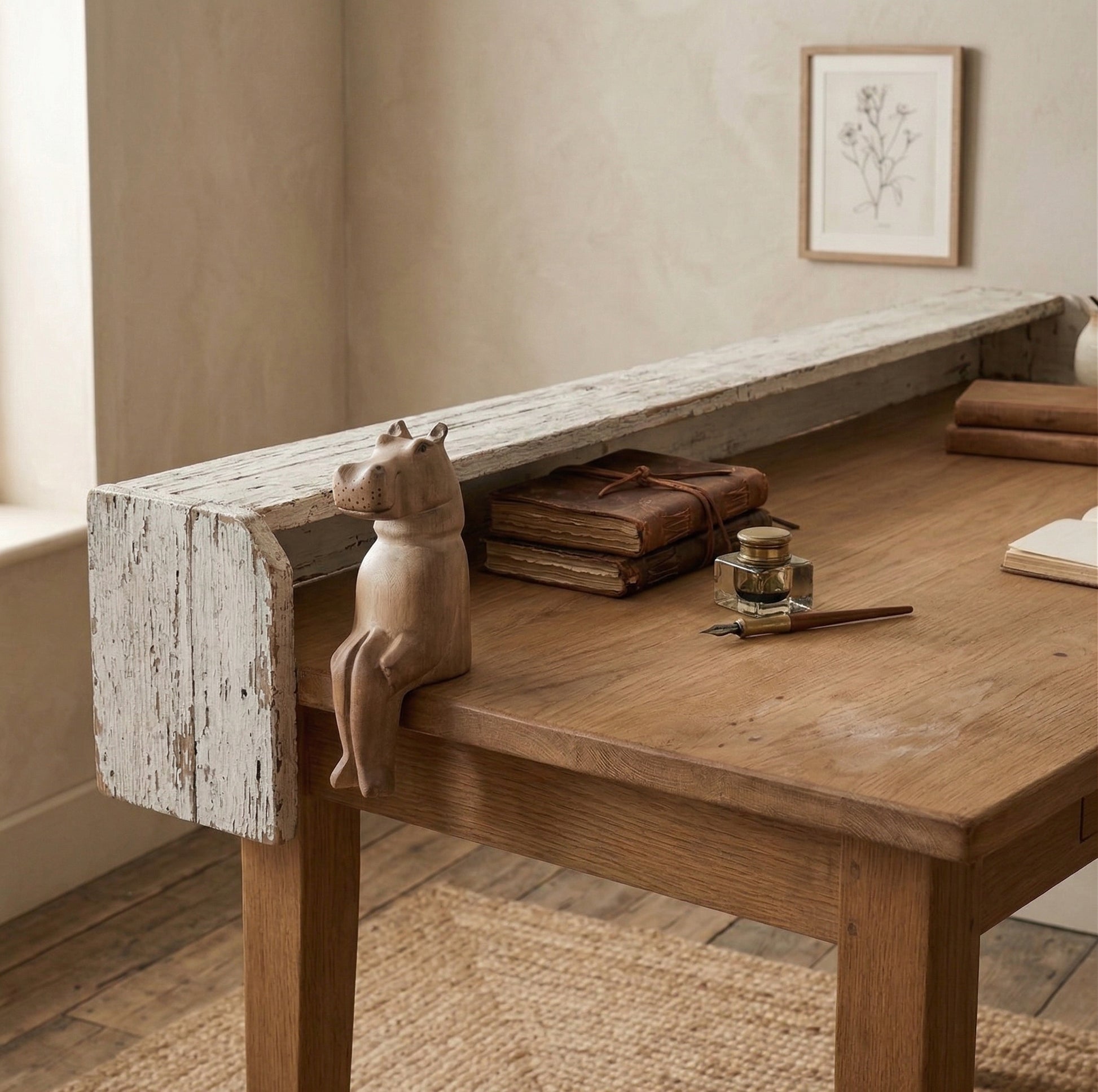 The Resting Hippo hand-carved wooden shelf sitter perched on the edge of a rustic oak desk beside leather-bound journals and an ink well, showing seated pose and natural wood finish, carved by Kamba tribe artisans in Kenya