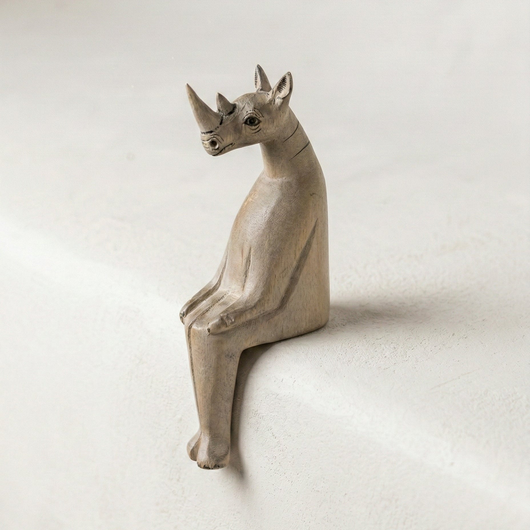 The Resting Rhino hand-carved wooden shelf sitter showing painted detail and wood grain texture against a neutral background