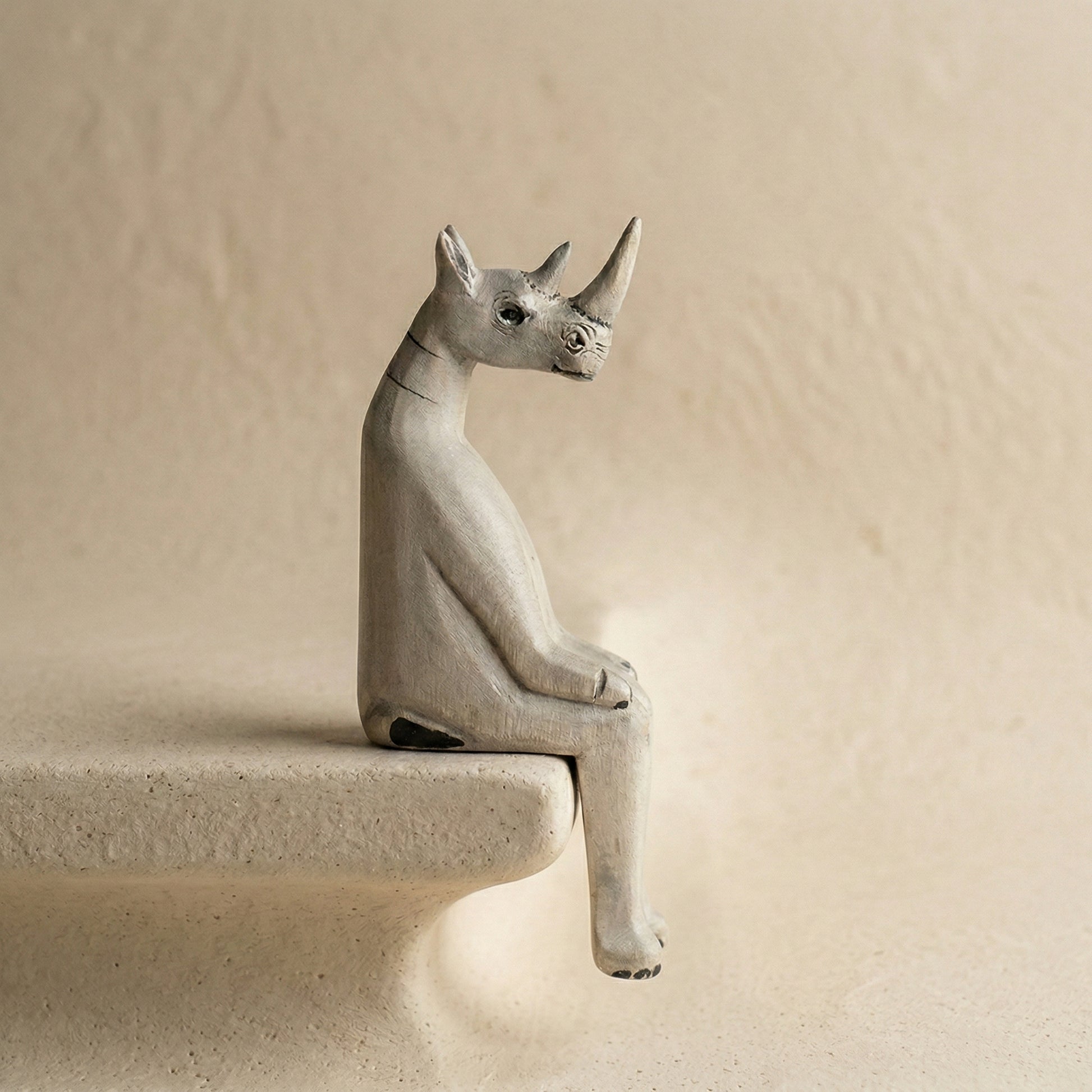 The Resting Rhino hand-carved wooden shelf sitter in a seated pose with dangling legs, carved from jacaranda wood by Kamba tribe artisans in Kenya, from WILLAGE