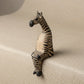 The Resting Zebra hand-carved wooden shelf sitter in a seated pose, with painted black and white stripes, carved by Kamba tribe artisans in Kenya, from WILLAGE