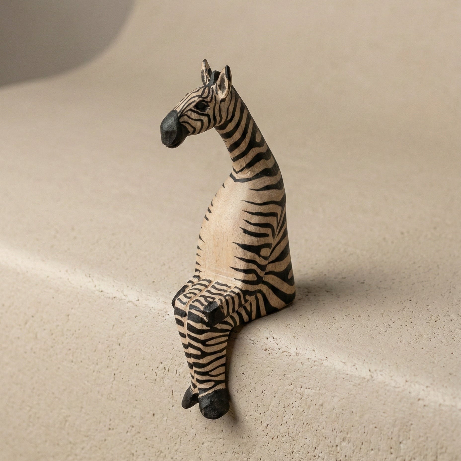 The Resting Zebra hand-carved wooden shelf sitter in a seated pose, with painted black and white stripes, carved by Kamba tribe artisans in Kenya, from WILLAGE