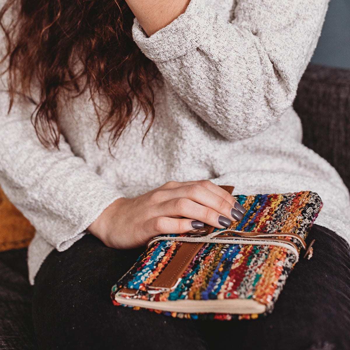 Hand resting on a closed woven sari journal with leather strap and wrap tie, showing its size in a lap