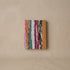 Pocket journal with a woven cover of multicolour upcycled sari strips in pink, teal, white, plum and green, with a tan leather edge, against a plaster wall