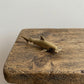 The Silent Navigator miniature brass hammerhead shark on a wooden surface, showing distinctive wide head and warm aged patina, from the WILLAGE Tiny Objects collection