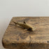 The Silent Navigator miniature brass hammerhead shark on a wooden surface, showing distinctive wide head and warm aged patina, from the WILLAGE Tiny Objects collection
