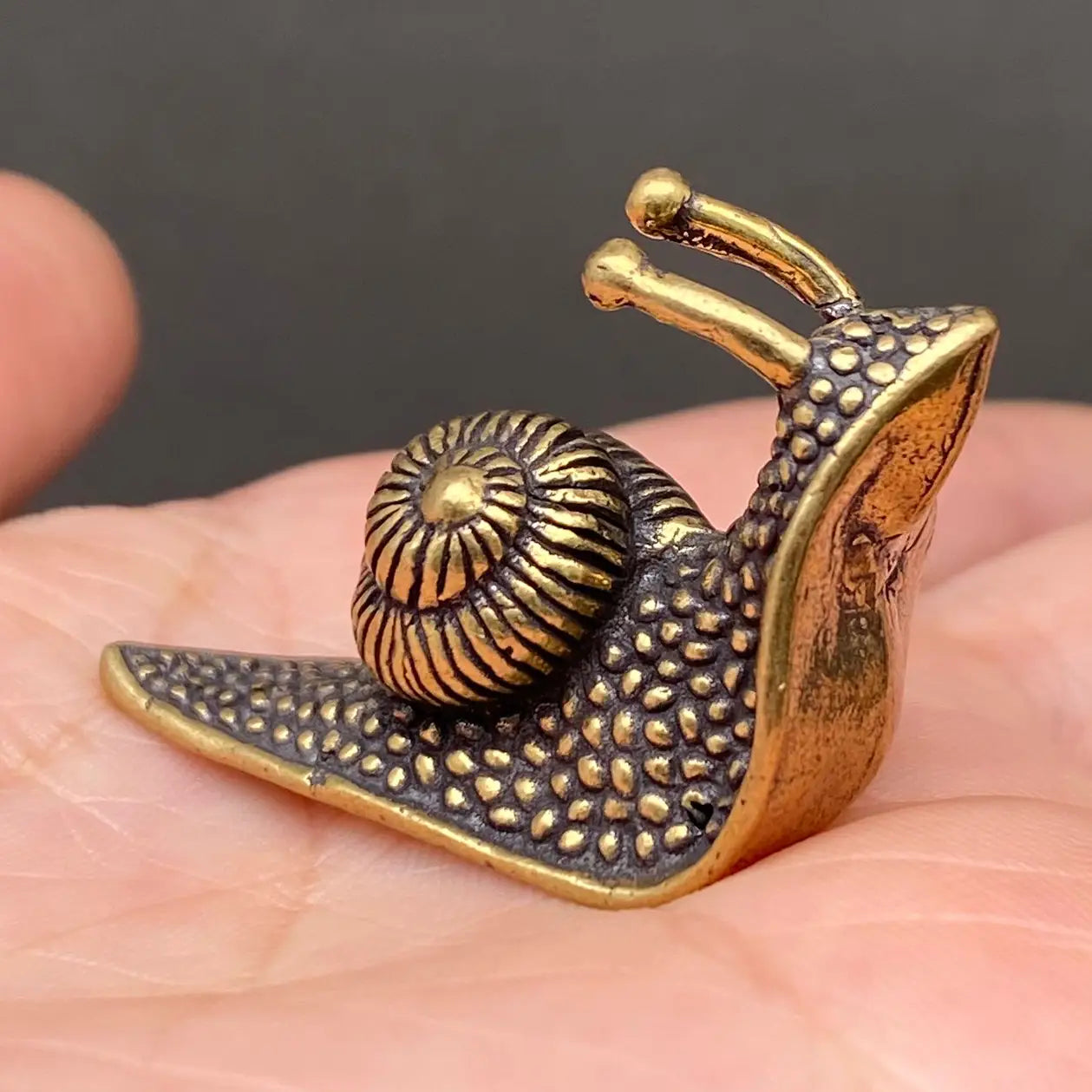 The Slow Path miniature solid brass snail figurine with a striped spiral shell and dotted texture, held in a hand