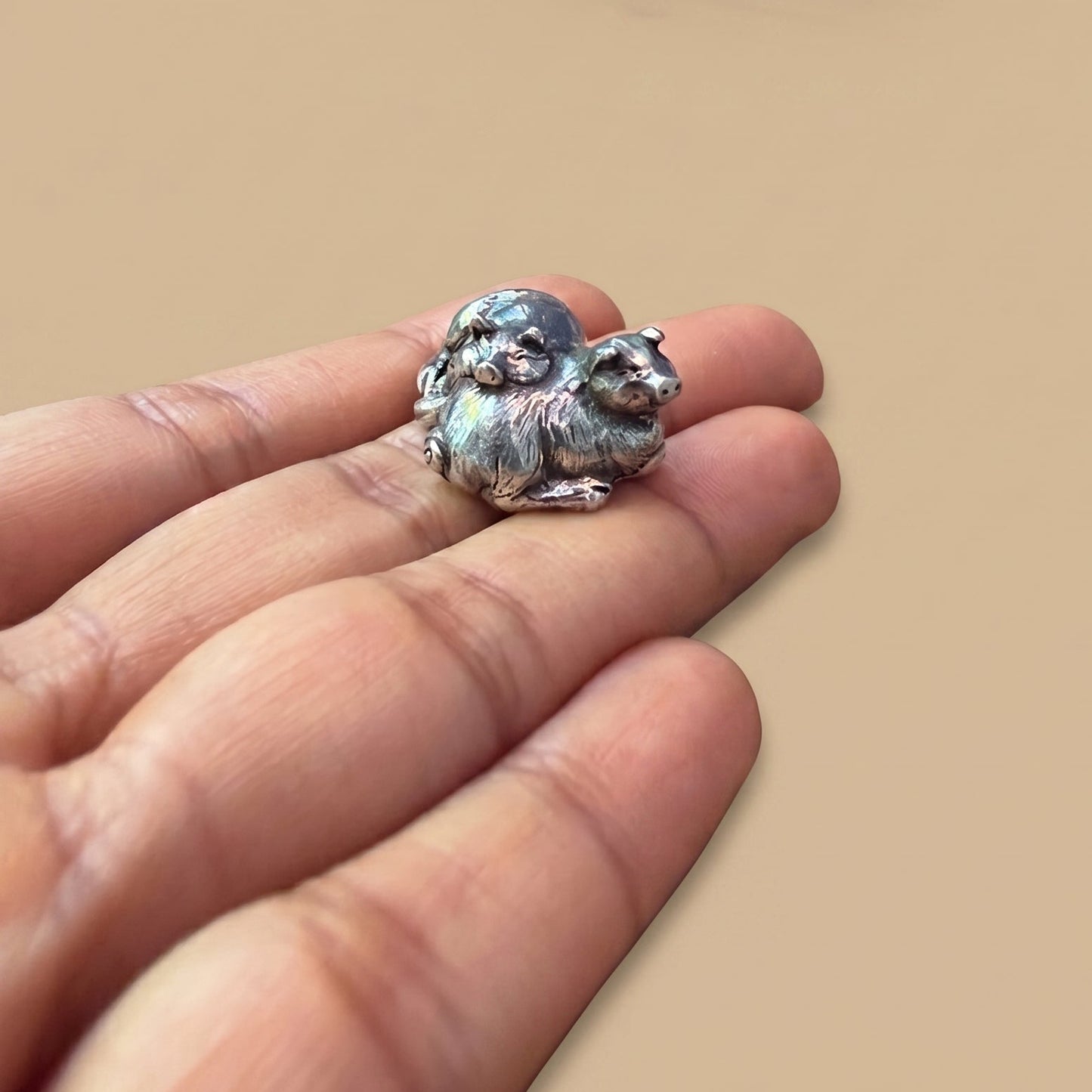 Tiny pewter figurine of two sleeping pigs resting on fingertips, showing its miniature scale