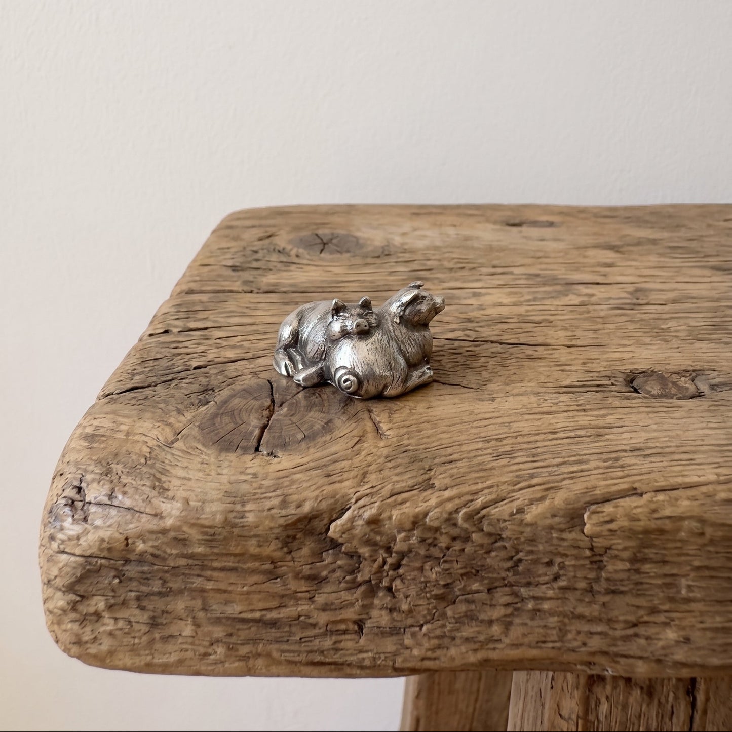 Pewter figurine of two pigs sleeping against each other with detailed coats, on a rustic wooden surface