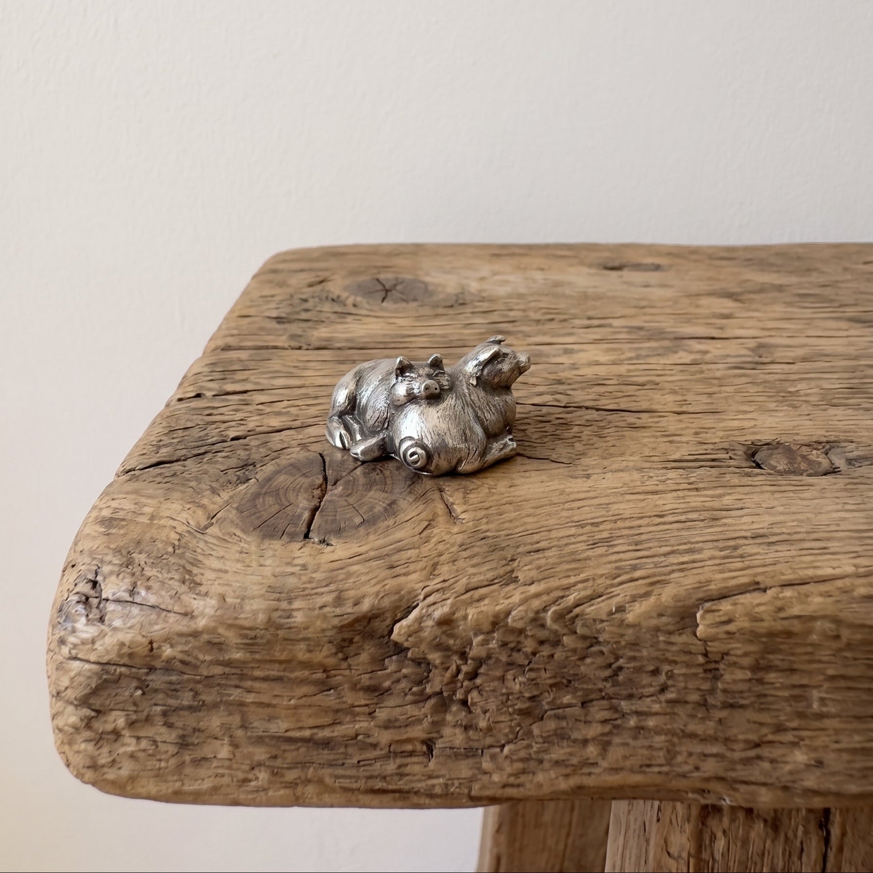 Pewter figurine of two pigs sleeping against each other with detailed coats, on a rustic wooden surface