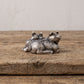 Small pewter sleeping pigs figurine displayed on the corner of a weathered wood bench