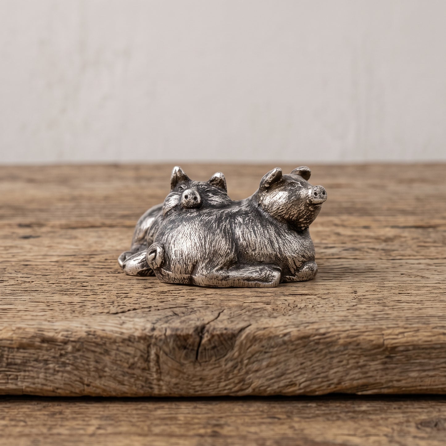 Small pewter sleeping pigs figurine displayed on the corner of a weathered wood bench