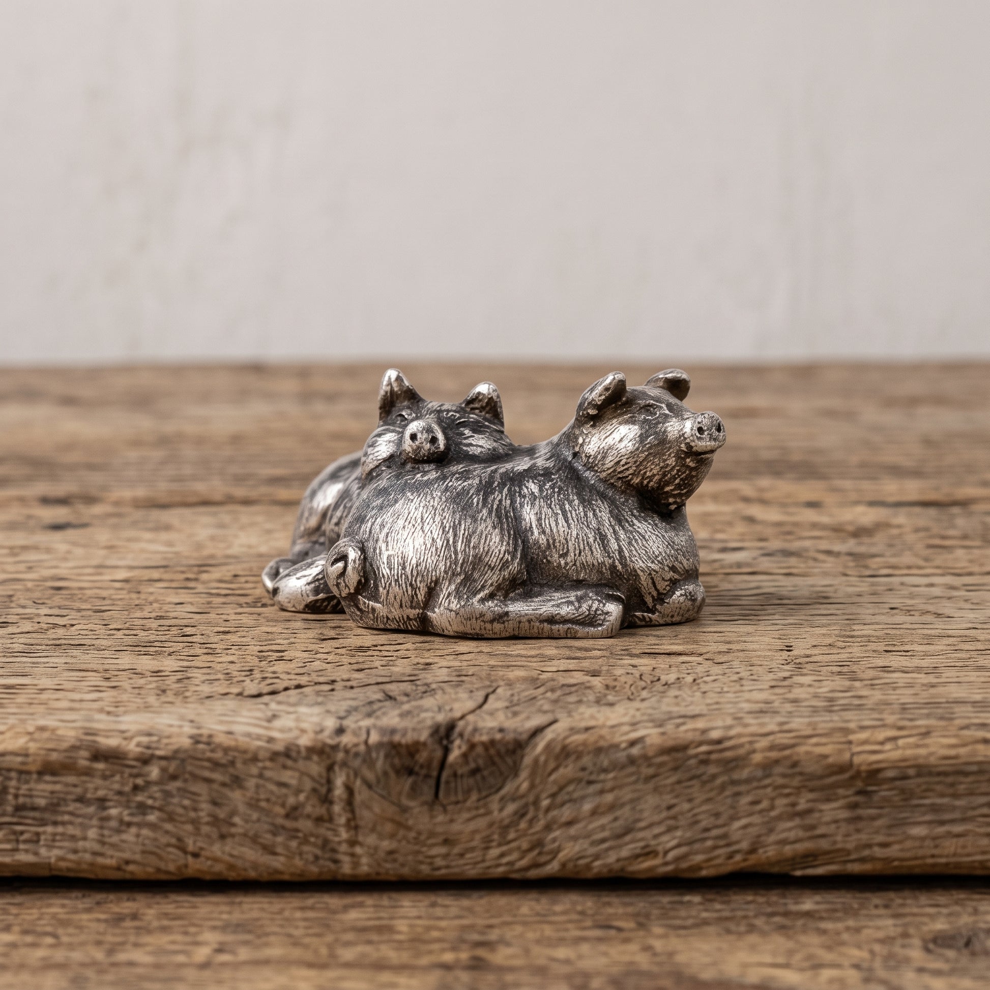 Small pewter sleeping pigs figurine displayed on the corner of a weathered wood bench