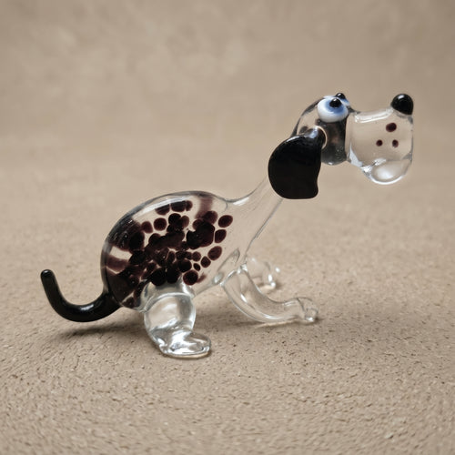 Front-angled view of The Spotted Sprinter lampworked glass dog figurine showing face detail with blue eyes, black nose, and purple-black spots in clear solid glass, by Glass by Iness
