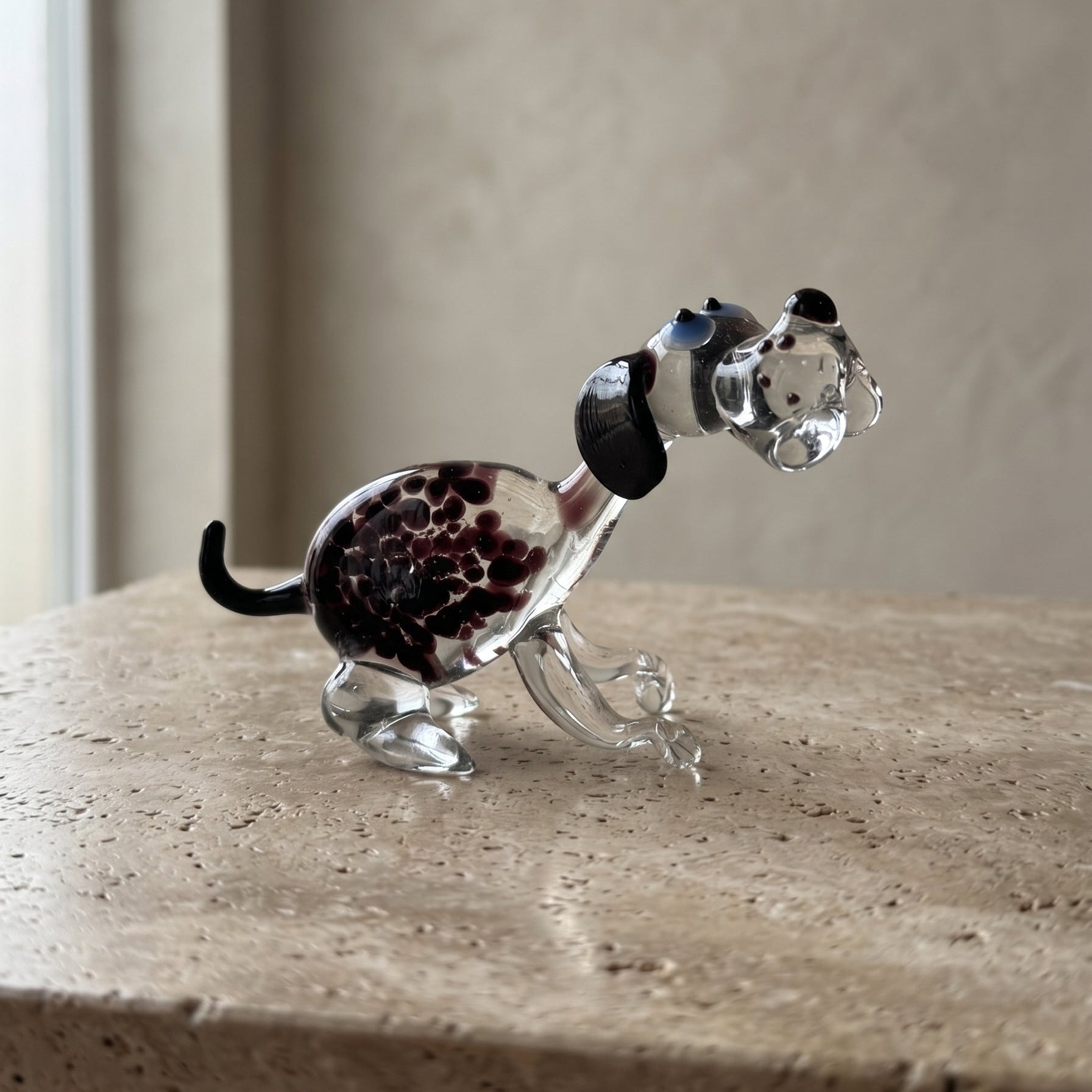 The Spotted Sprinter lampworked glass dog figurine shown next to a U.S. quarter for scale on a rustic wood beam, solid Ukrainian glass with purple-black spotted pattern
