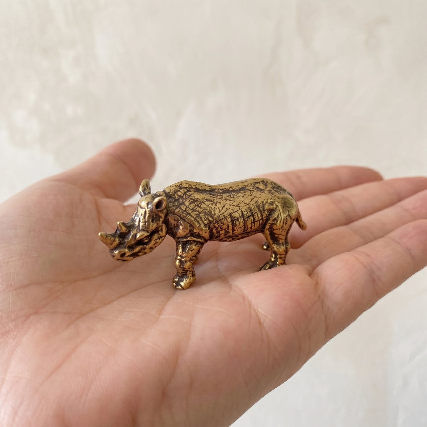 The Stand brass rhino held in a hand to show its small size, about 2 inches long