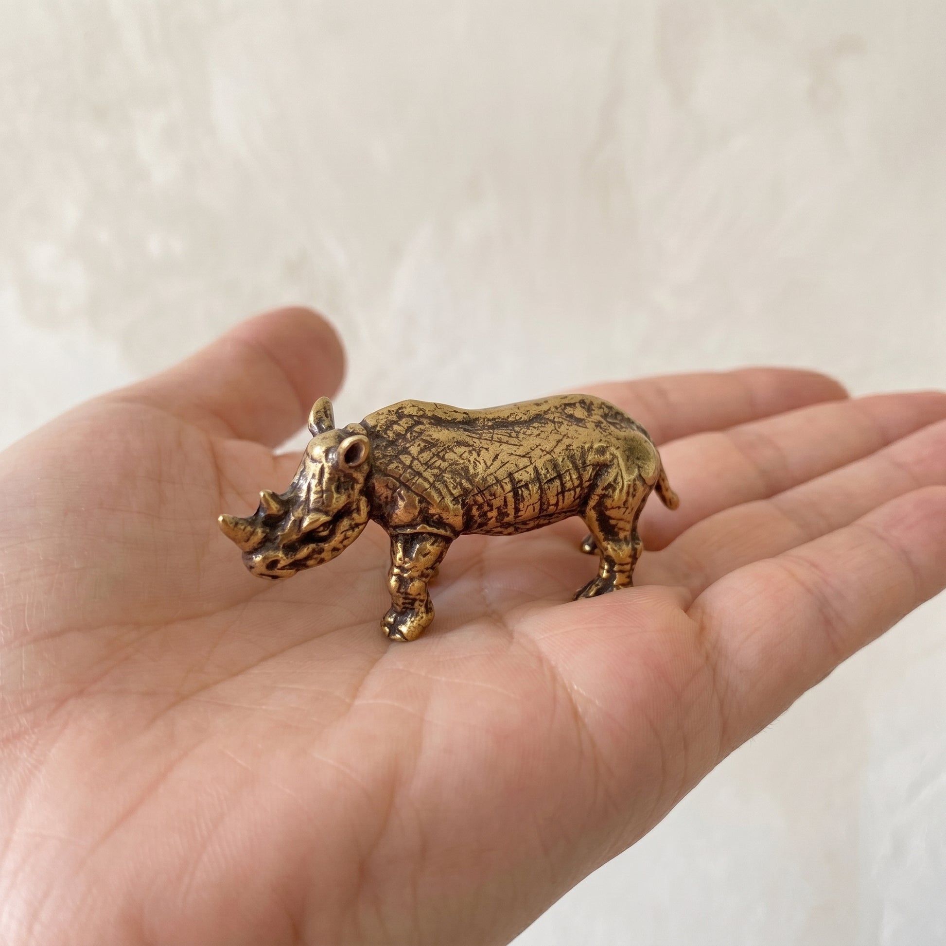 The Stand brass rhino held in a hand to show its small size, about 2 inches long
