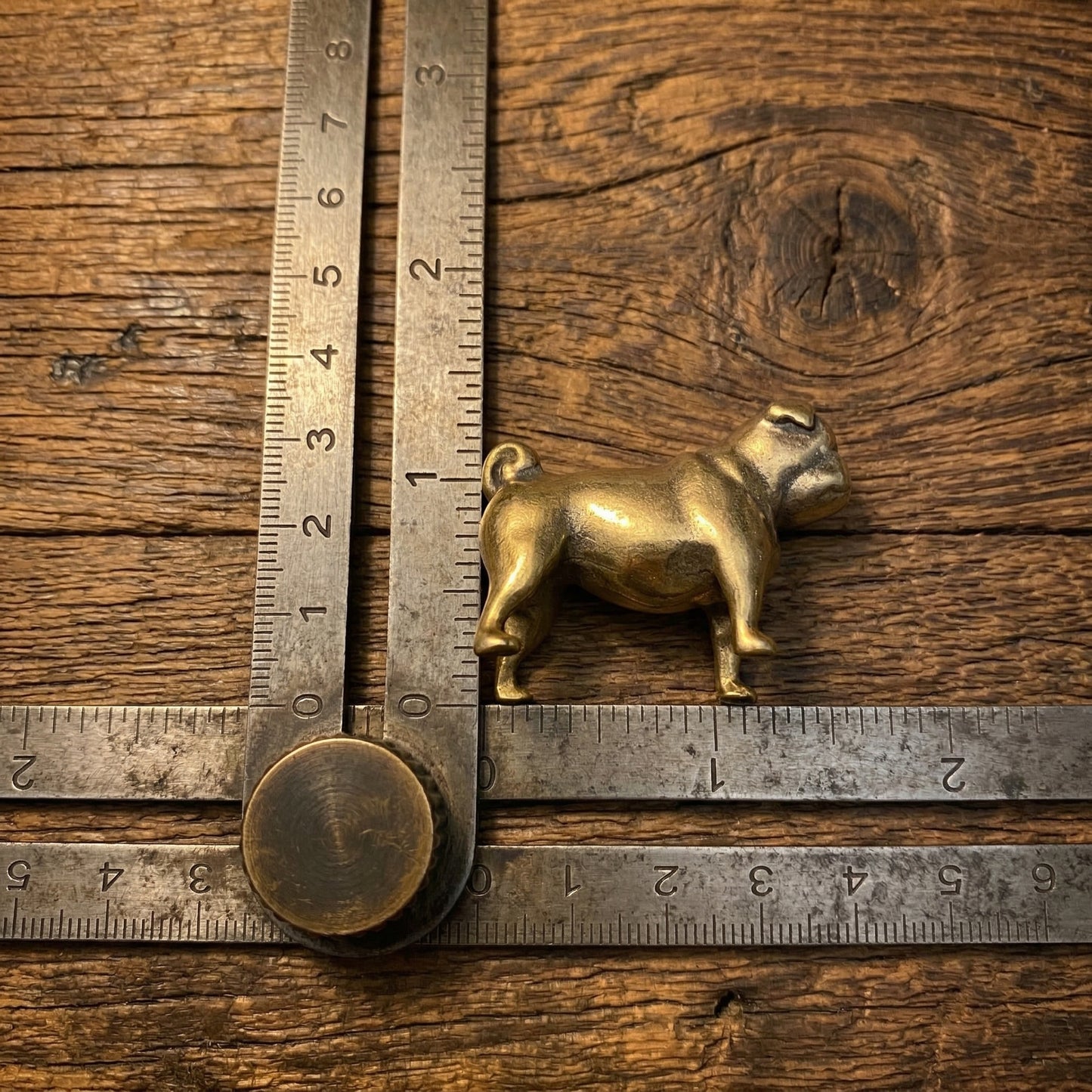 The Steadfast Companion miniature brass bulldog shown with ruler for scale, approximately 40 mm long, on a wooden surface