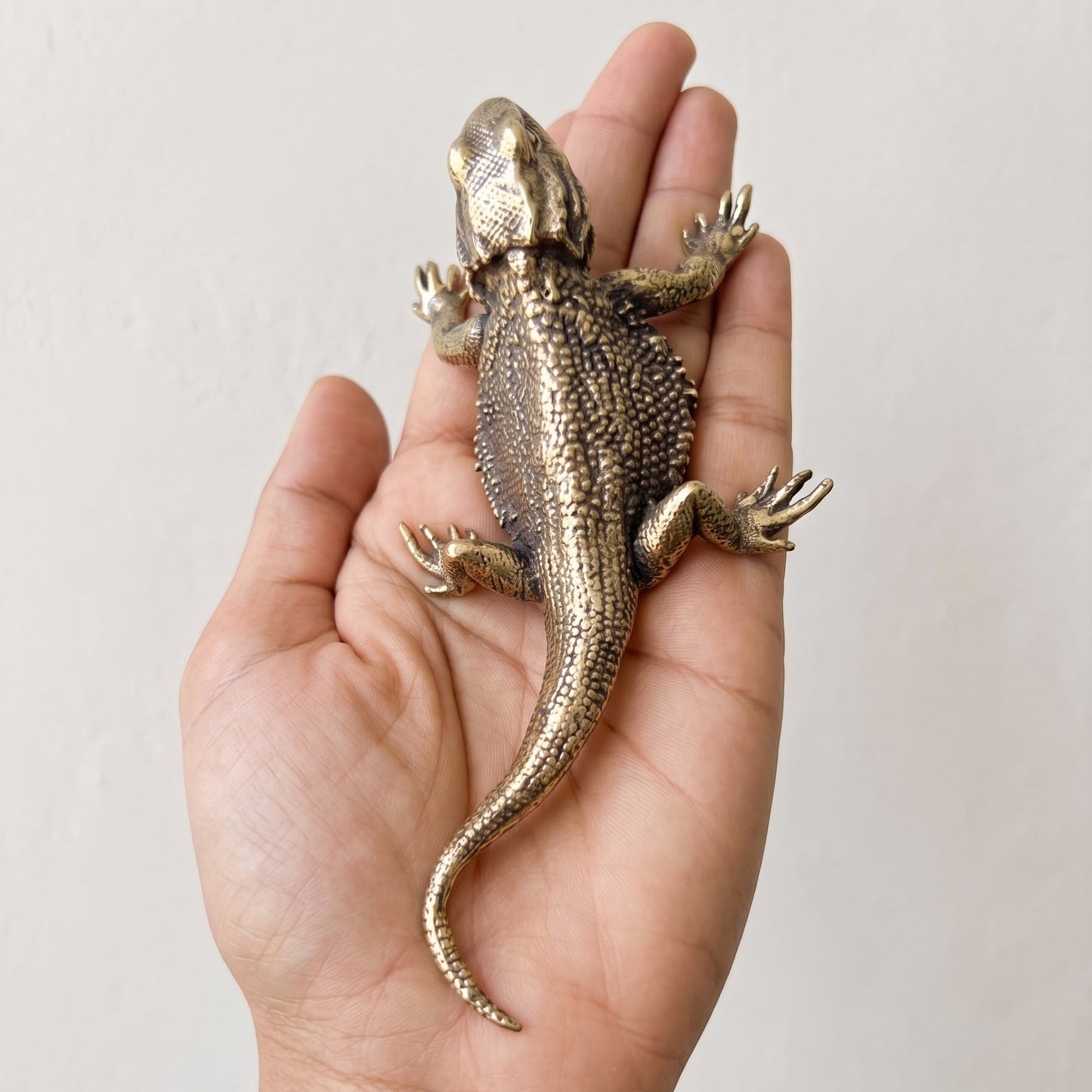 Brass bearded dragon figurine resting in an open hand to show its palm-length scale and weight