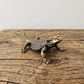 Side view of a brass bearded dragon figurine showing the raised head, scaled flank, and long tapering tail