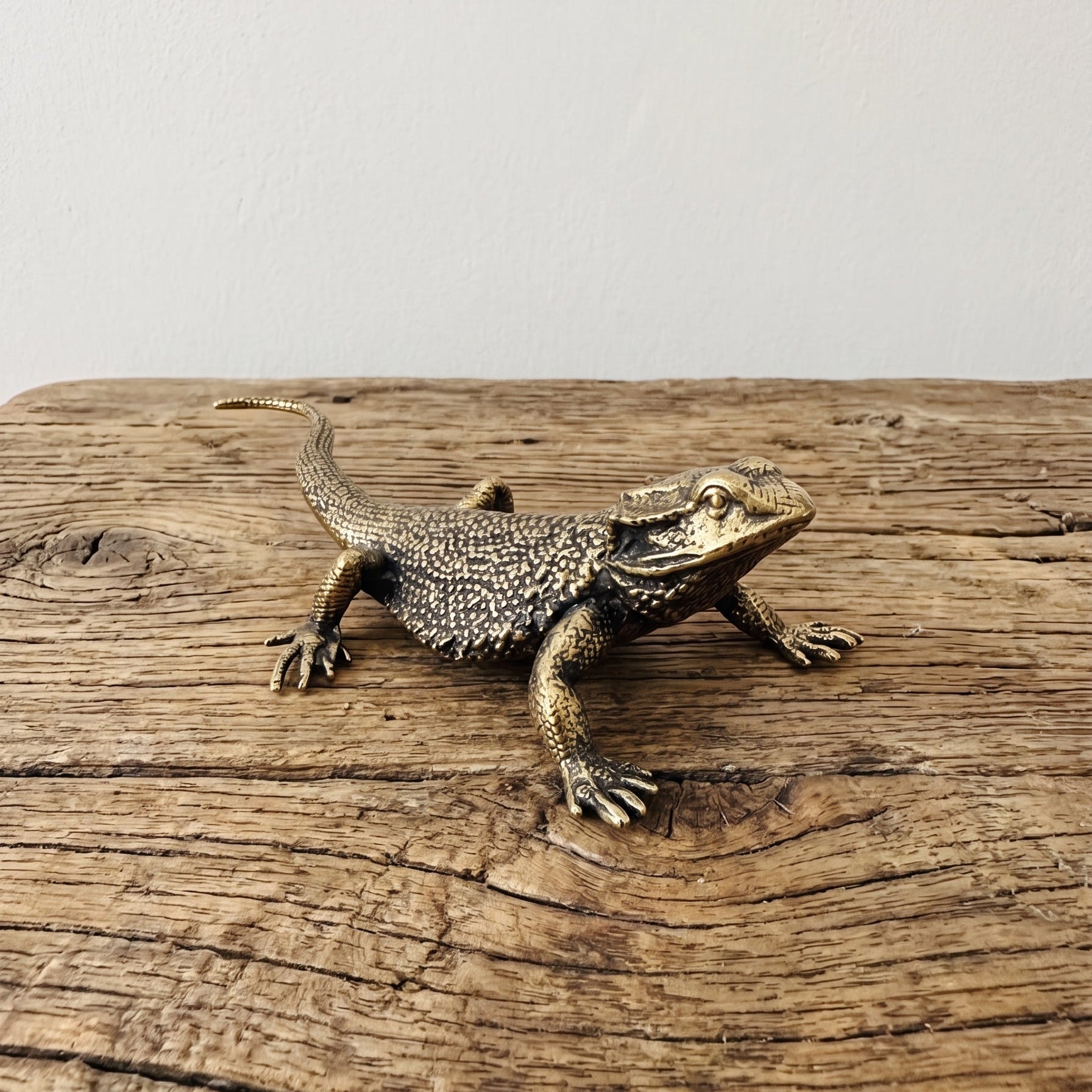 Side view of a brass bearded dragon figurine showing the raised head, scaled flank, and long tapering tail