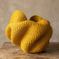 Front view of a yellow Bolga basket showing its wide, petal-like folded opening and fine coiled weave