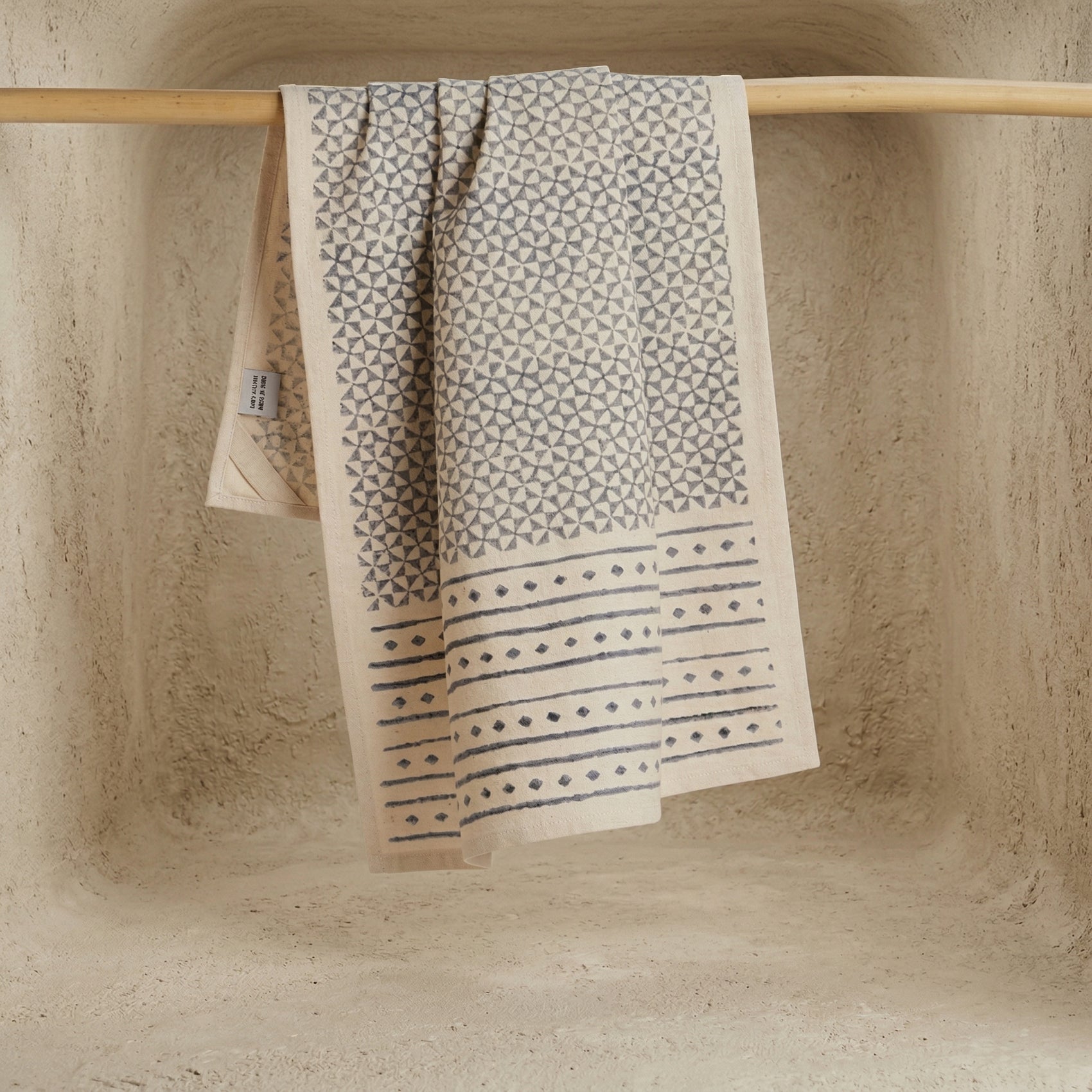 The Pattern hand block printed kora cotton kitchen towel in natural and slate grey hanging on wooden rod