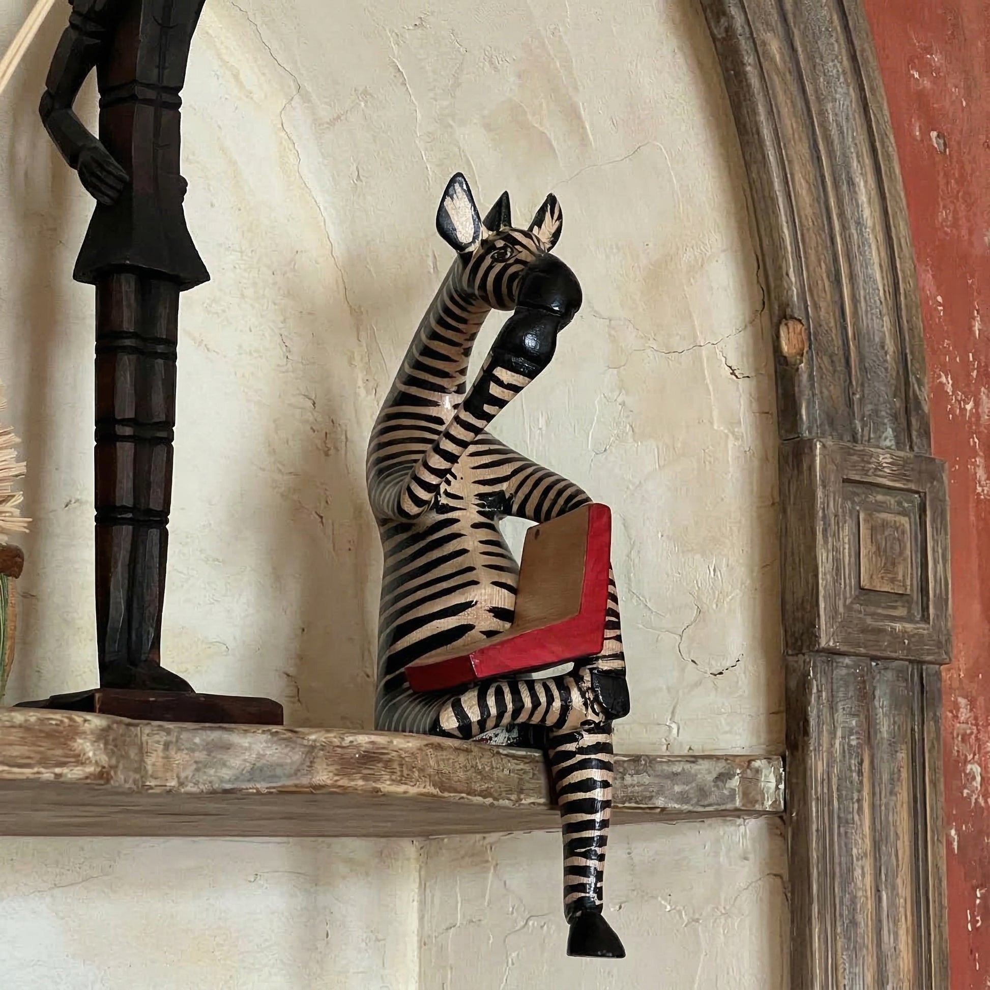 and-carved thinking zebra wood sculpture perched on decorative shelf showing 3-inch sitting notch and dangling leg