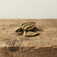 The Tidal Wanderer miniature brass sea turtle held in hand to show scale, with detailed flippers and golden patina