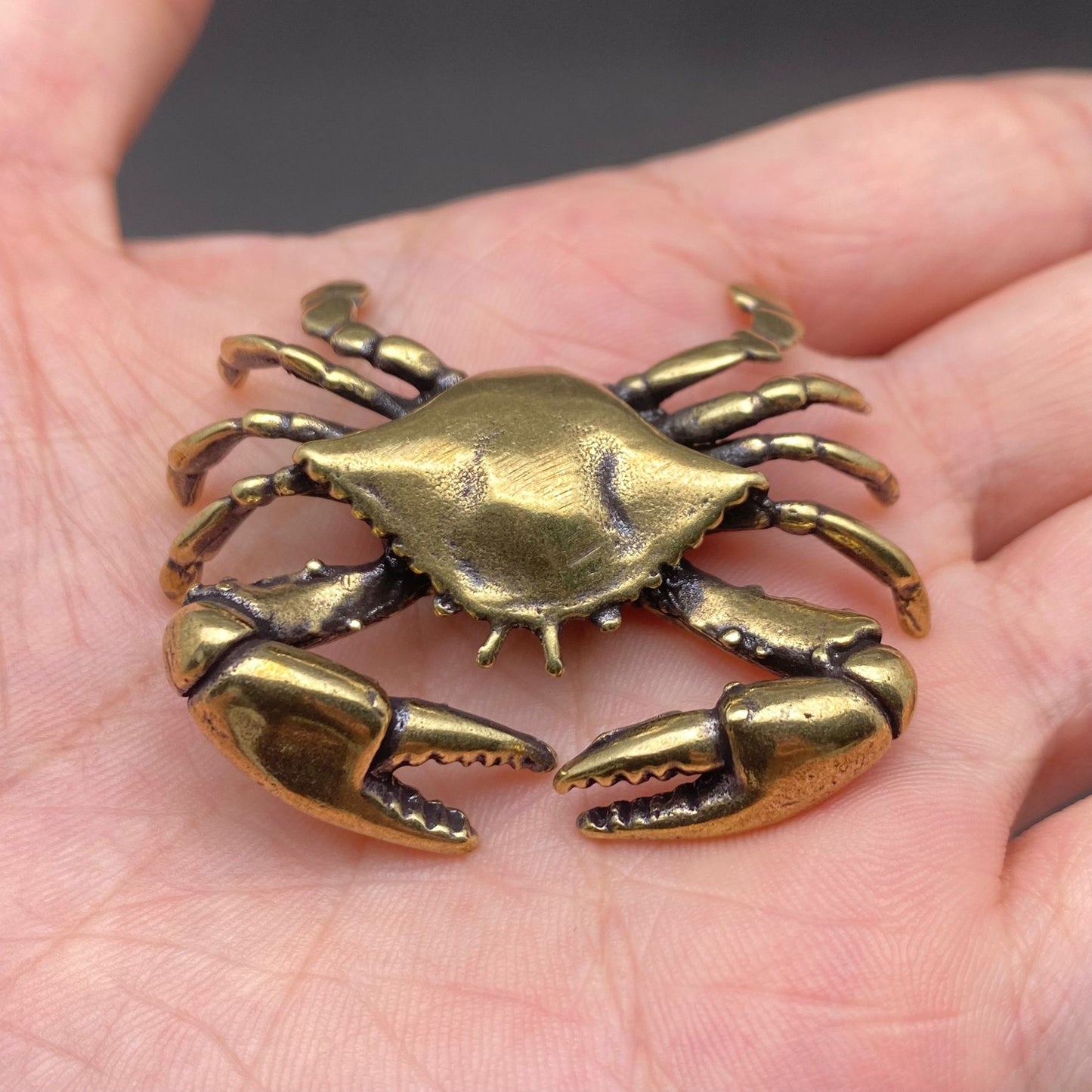 The Tide Keeper brass crab held in a hand to show its small size, solid brass with warm patina