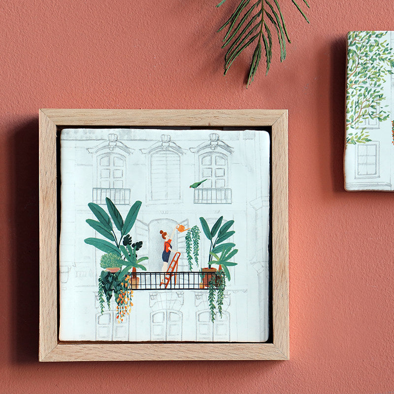 Urban Jungle Storytile framed and displayed on a warm-toned wall showing illustrated balcony garden, hand-baked ceramic by Marga van Oers in the Netherlands, from WILLAGE