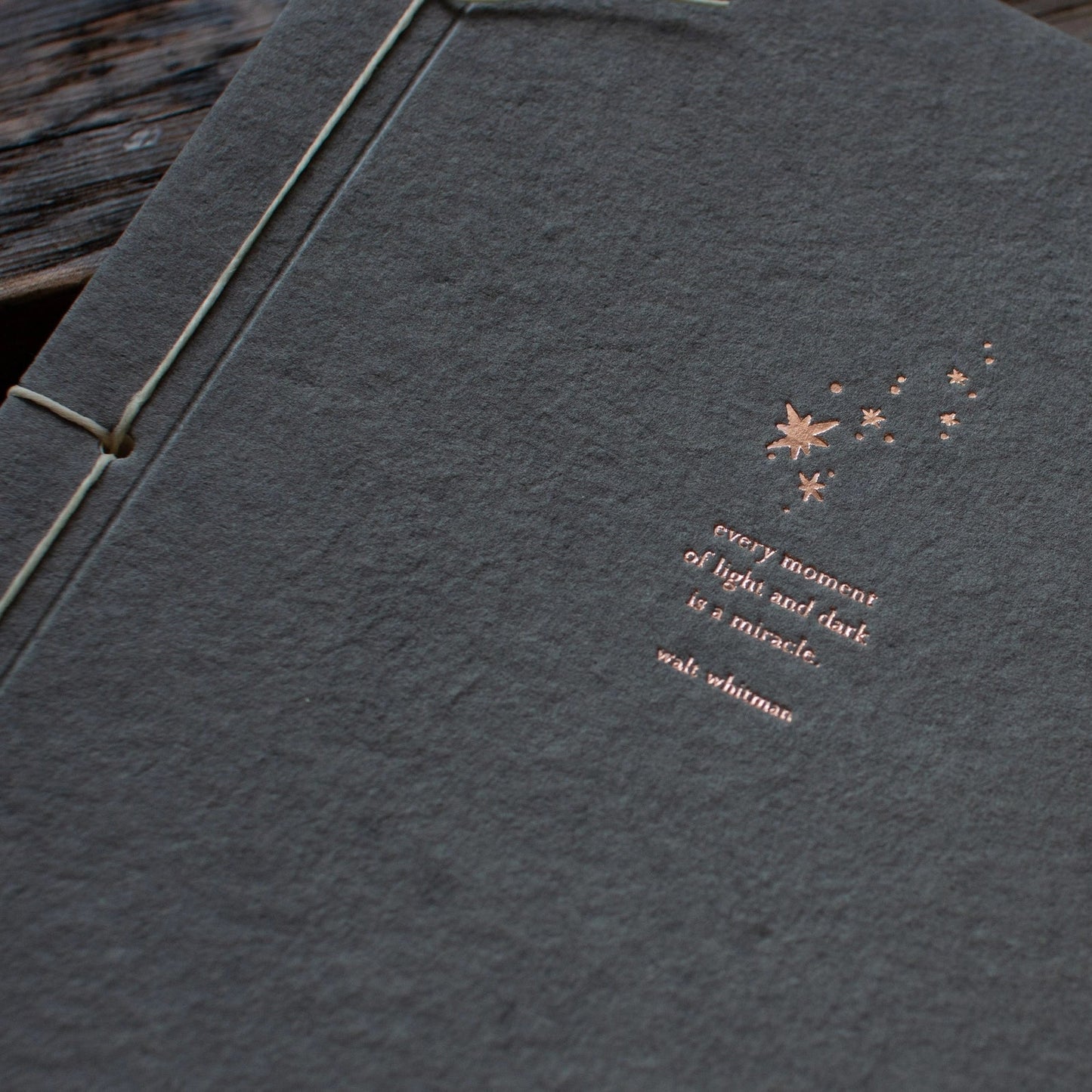 Close-up of copper foil letterpress constellation and Walt Whitman quote on charcoal handmade paper journal cover