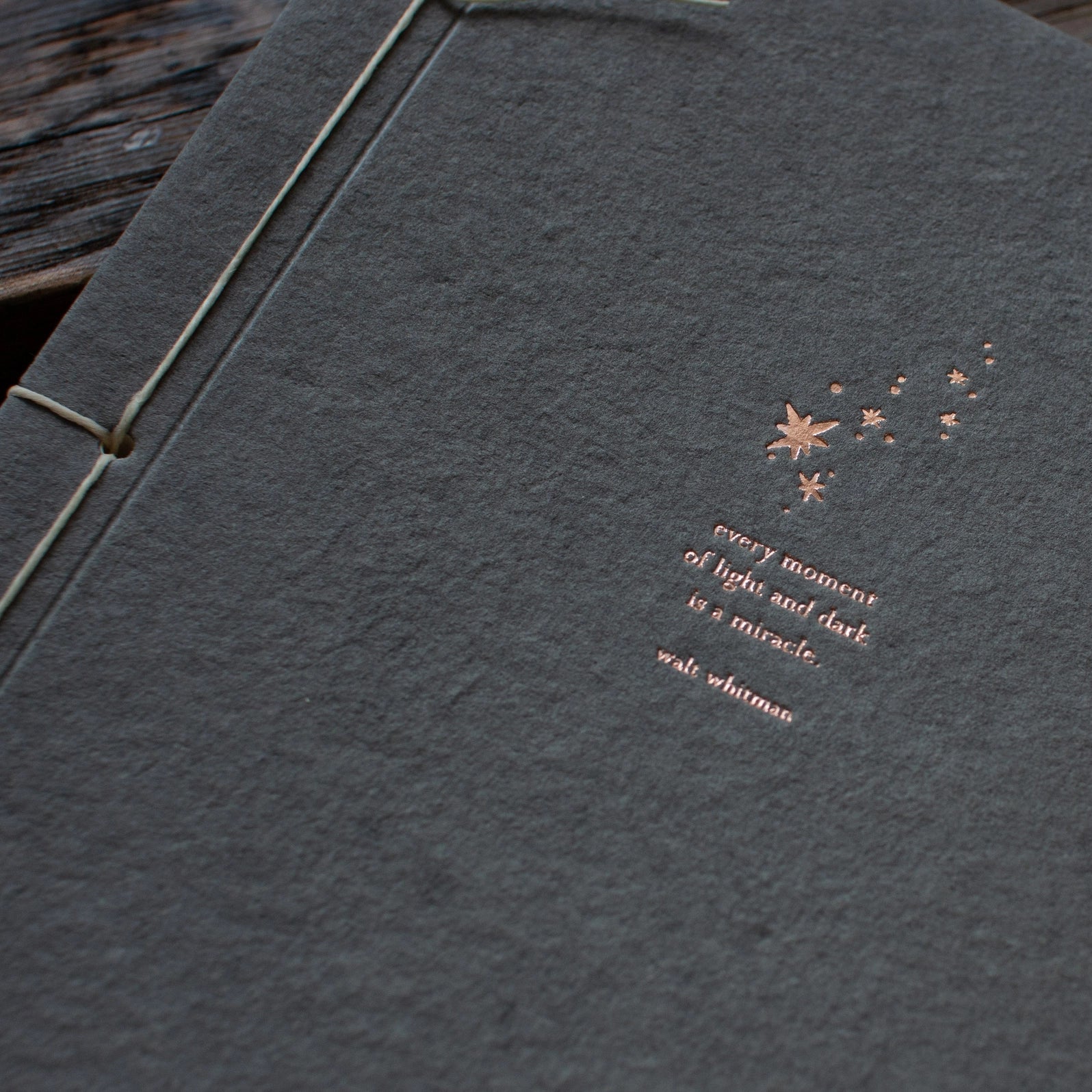 Close-up of copper foil letterpress constellation and Walt Whitman quote on charcoal handmade paper journal cover