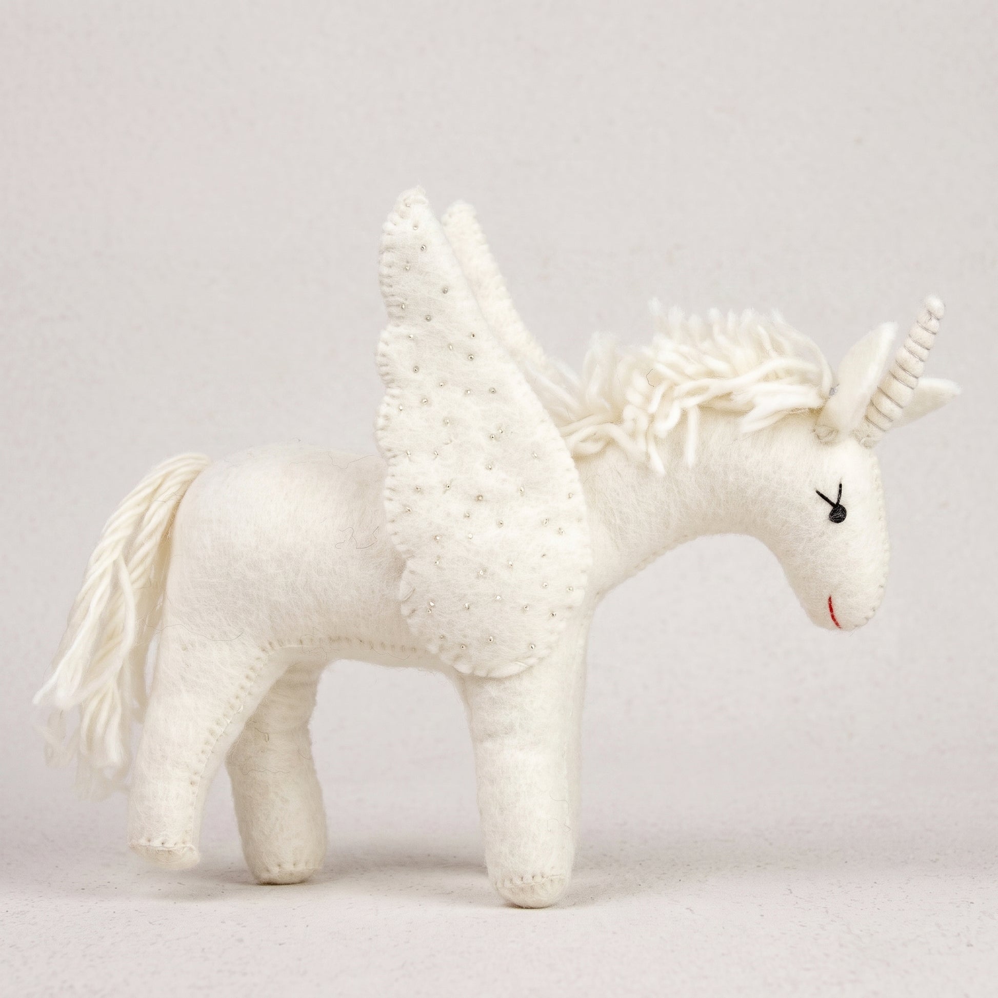 All-white hand-felted unicorn with beaded wings, a floss mane and spiralled horn, on a white background