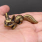 The Watchful Spirit miniature brass fox in a seated alert pose on a wooden surface, with warm aged patina, from the WILLAGE Tiny Objects collection
