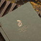 Close-up of copper foil letterpress compass and Wendell Berry quote on olive handmade paper journal cover
