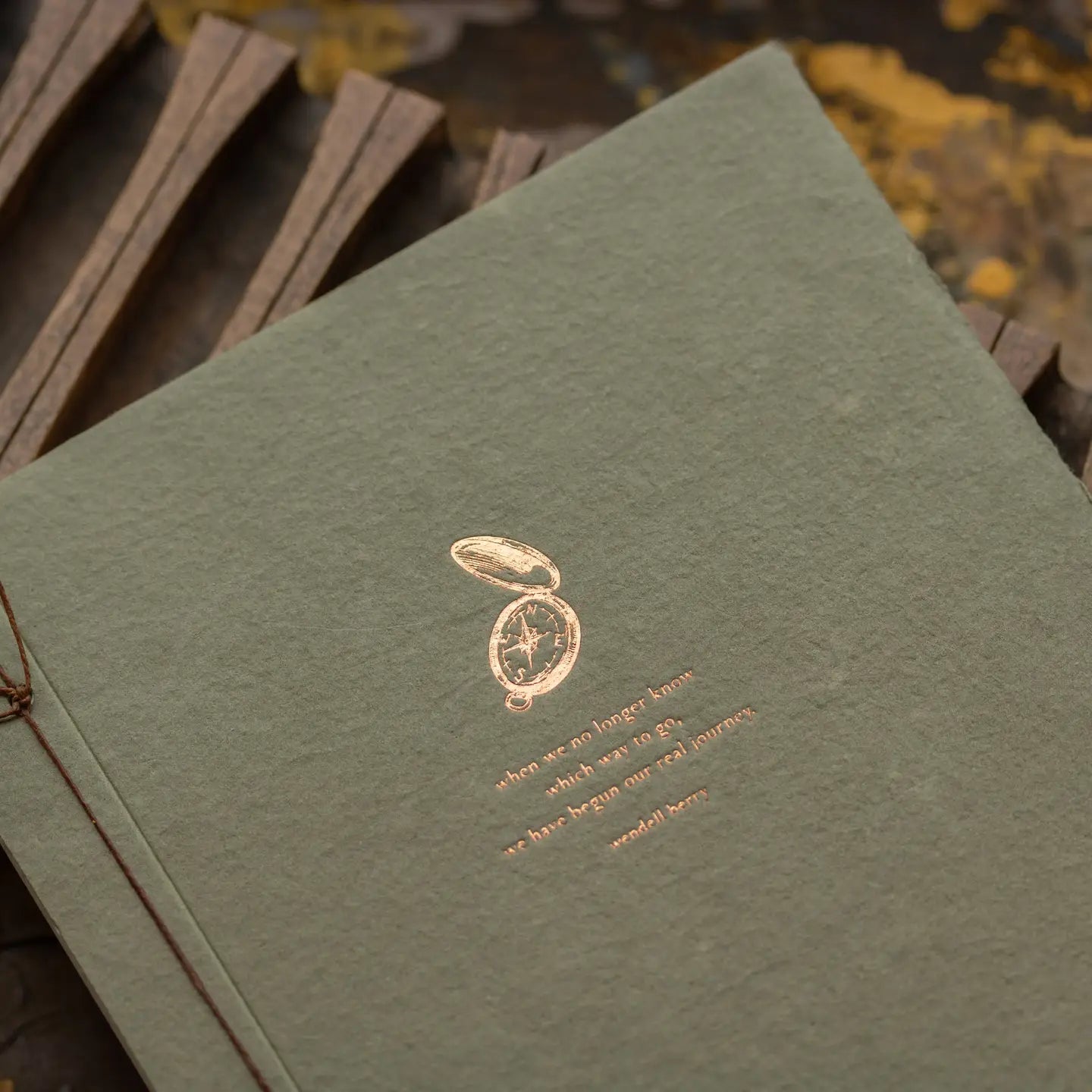 Close-up of copper foil letterpress compass and Wendell Berry quote on olive handmade paper journal cover