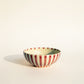 Ceramic bowl with red and white striped pattern on a beige background