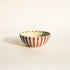 Ceramic bowl with red and white striped pattern on a beige background