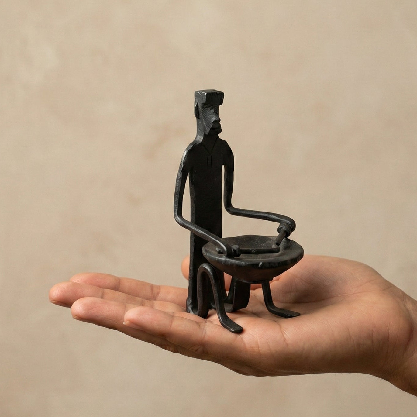 Hand holding a small black sculpture against a beige background