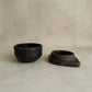 Two dark brown ceramic bowls on a light beige background