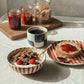Breakfast setting with a bowl of cereal, coffee, and bread with jam on a tablecloth.