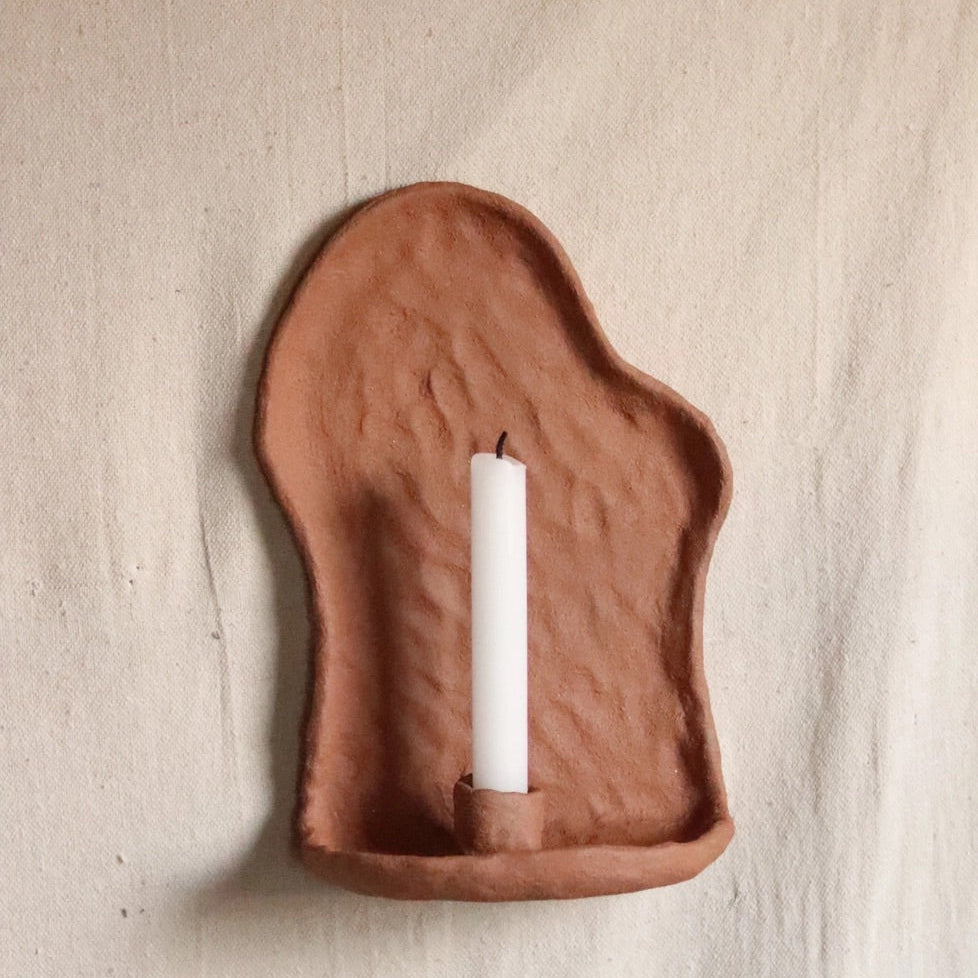 clay wall-mounted candle holder with a white candle on a beige background