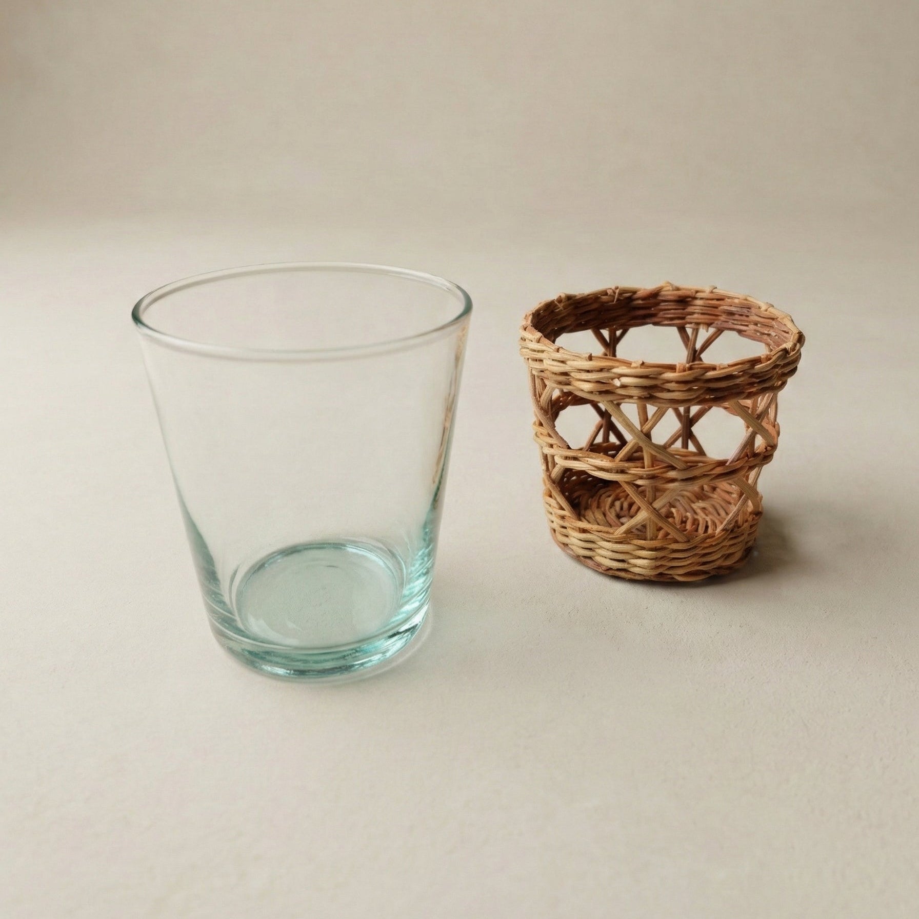 Clear glass tumbler and woven basket on a neutral background