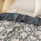 Reversible Ophelia linen quilt shown from stripe side on styled bed, demonstrating two-pattern versatility
