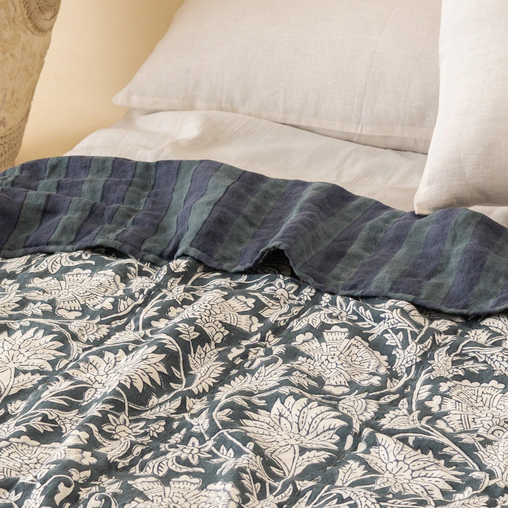 Reversible Ophelia linen quilt shown from stripe side on styled bed, demonstrating two-pattern versatility